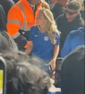 Woman in Chelsea jersey speaking with security guard in crowded stadium.