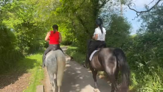 Two women horseback riding on a path.