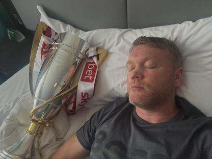 Man sleeping in bed next to a trophy.