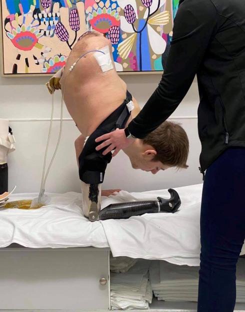 Loren Schauers, a man with amputated lower body, leaning forward on a bed with assistance.