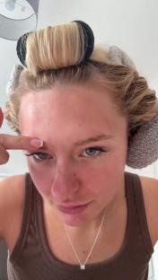 Woman with hair rollers touching her forehead.