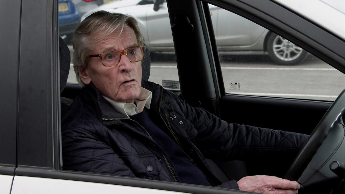 Ken Barlow in a car, appearing worried.