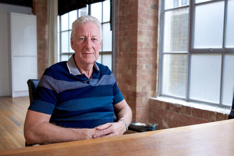 Photo of Ian Floyd sitting at a desk in a room with exposed brick walls.