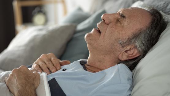 Older man sleeping in bed with mouth open.