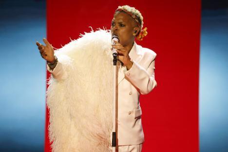 A singer in a white suit and feathered boa performs on stage.