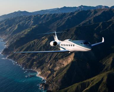 Private jet flying over mountains and ocean.
