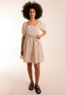Woman in a cream puff-sleeve mini dress with black pattern.