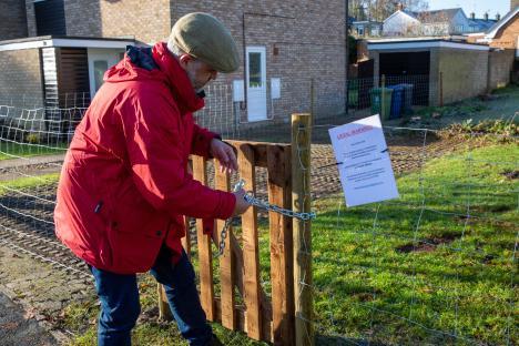Man securing a gate with a chain and lock.
