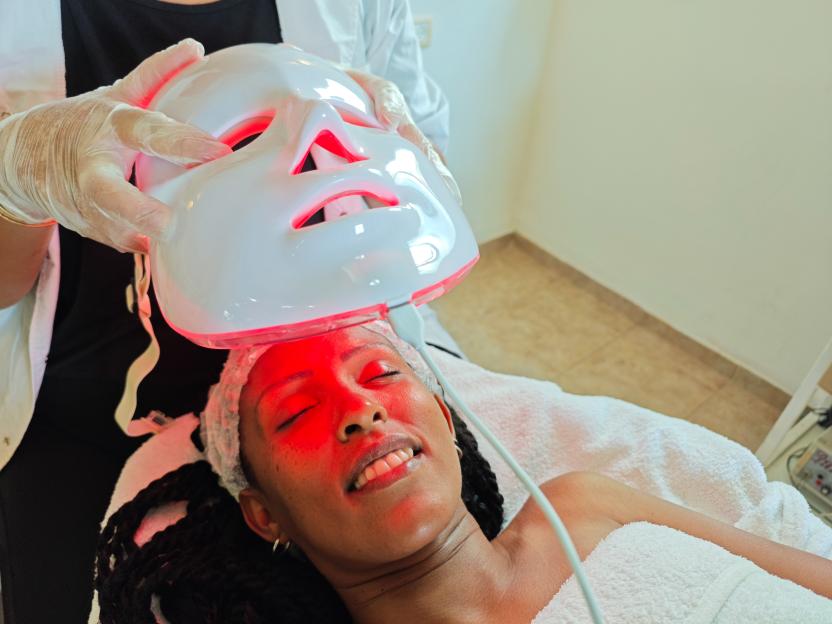 Aesthetician applying red LED light therapy mask to client's face.