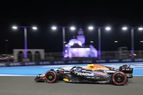 Max Verstappen's Red Bull car speeding on a racetrack at night.
