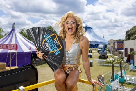 Drag queen Kitty Scott Claus holding a Grindr Rides Europe 2025 fan.