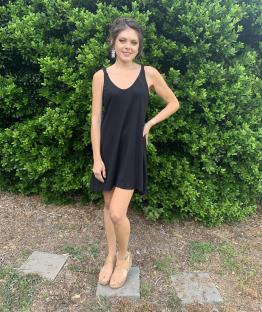 Woman in black dress standing in front of a green bush.