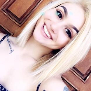 Portrait of a smiling young woman with blonde hair and tattoos.
