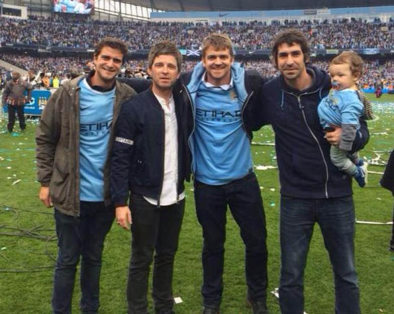 Noel Gallagher with four men and a baby at a soccer game.