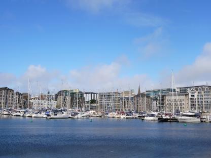 Plymouth waterfront with many boats moored and apartment buildings in the background.