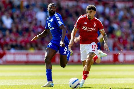 Soccer player in red jersey dribbling the ball past a player in a blue jersey.