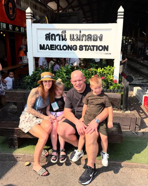 Michael van Gerwen with his family sitting on a bench in front of a sign for Maeklong Station.