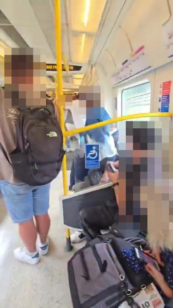 A man is being restrained by passengers on a crowded train.