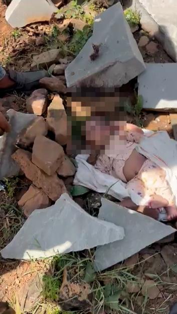 An abandoned baby with a stone in its mouth, surrounded by rocks and debris.