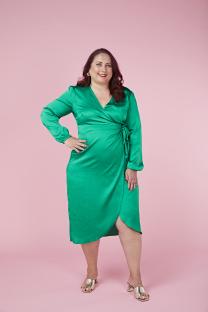 Woman in green dress smiling against pink background.