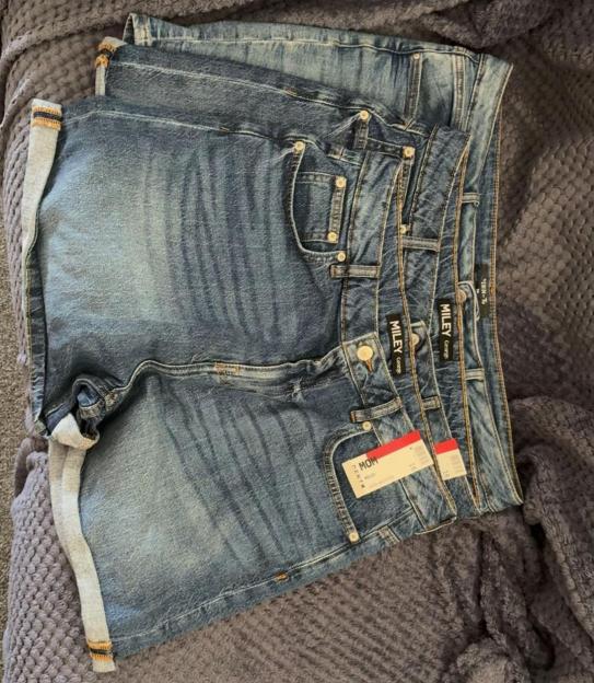 Three pairs of denim shorts stacked on a gray blanket.