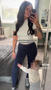 Woman taking a selfie in leggings, with a toddler touching her leg.