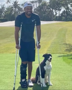 Tiger Woods on crutches with his dog on a golf course.