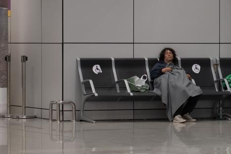 Homeless person sleeping on a bench at an airport.