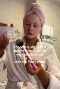 Woman demonstrating how to blend patchy fake tan using baby oil and a brush.