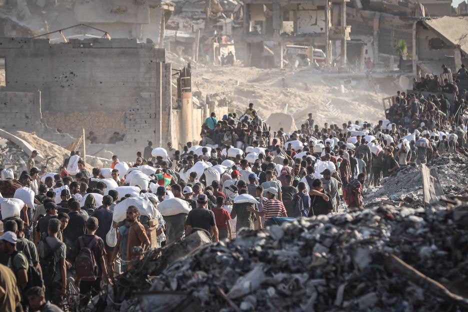 Palestinians carrying sacks of food aid through rubble in Gaza.