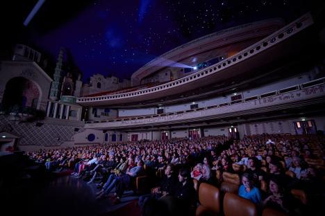 A large audience watching a film in a grand movie theater.