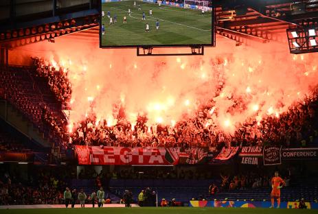 Legia Warsaw fans lighting flares in a stadium.