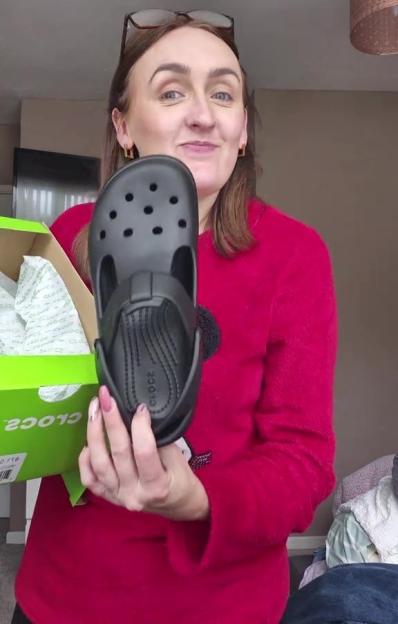 Woman holding up a black Croc shoe.