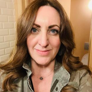 Photo of Mel Coloma, a woman with long brown hair, wearing a green jacket.