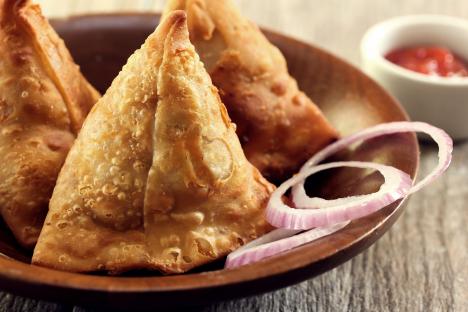 Fried samosas with red onion slices and sauce.