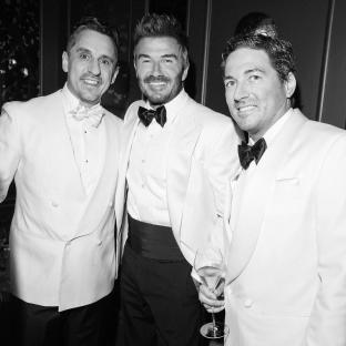 Black and white photo of David Beckham with two other men in white dinner jackets at his 50th birthday party.