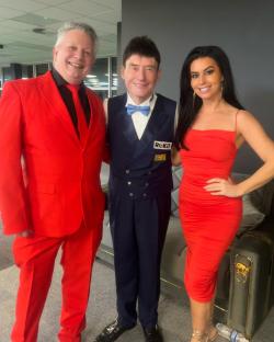 Three people posing for a photo; one in a red suit, one in a blue vest and dark trousers, and one in a red dress.