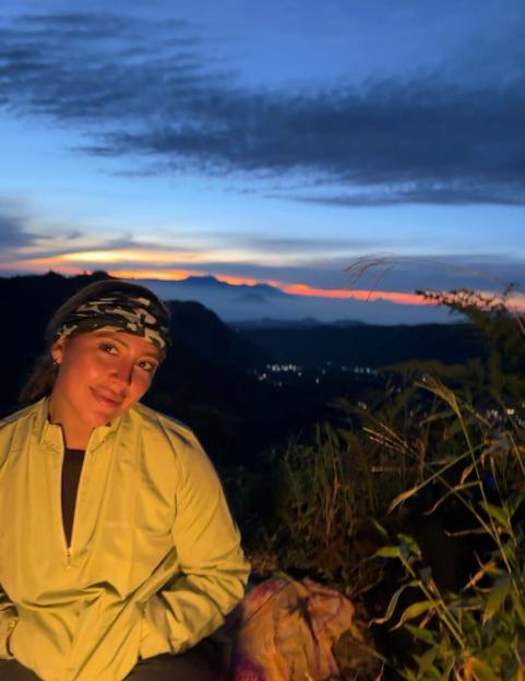 Woman sitting outdoors at dusk, looking at the camera.
