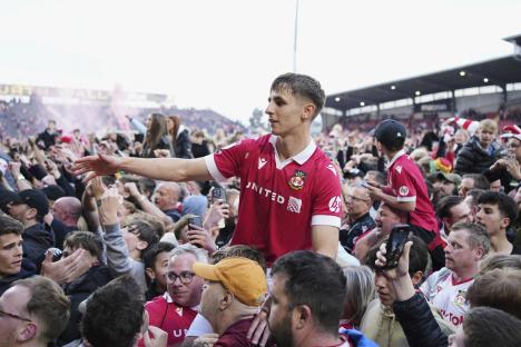 Wrexham's Max Cleworth celebrates with teammates and fans after a soccer match victory.