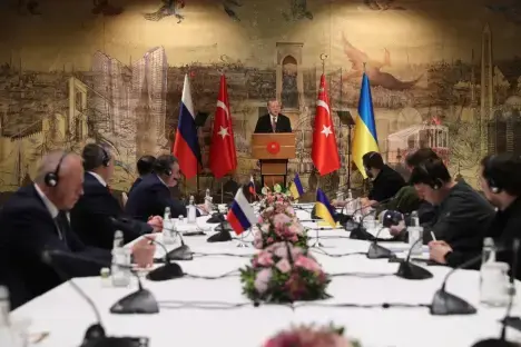Delegations from Russia and Ukraine meet at a table with Turkish President ErdoÃan speaking at a podium.