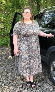 Woman in leopard print dress standing by car.