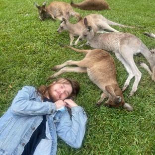 Man lying on grass surrounded by kangaroos.