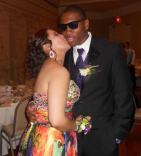 Woman in colorful dress kissing man in tuxedo at prom.