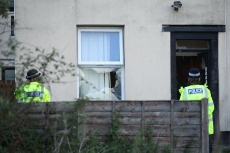 Police officers at a house with a broken window and door.