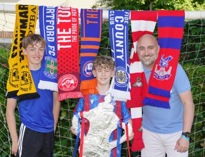 Father and two sons with football scarves, holding a replica FA Cup trophy.