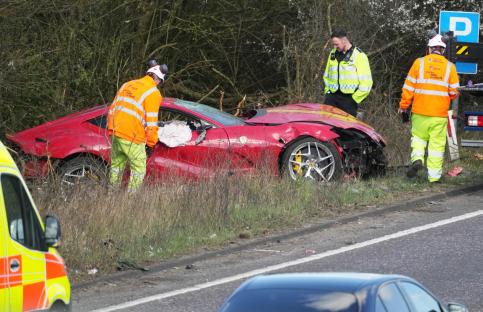 A wrecked red Ferrari on the side of a road with emergency personnel present.