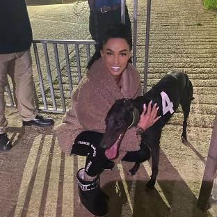 Woman crouching and hugging a racing greyhound wearing a racing bib with the number 4.