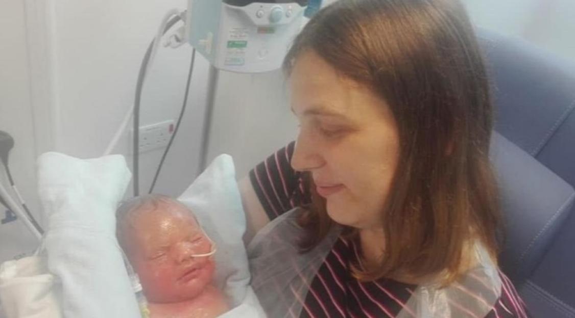 A woman looks at her newborn baby, Caiden, who is wrapped in a blanket, his skin red and irritated.