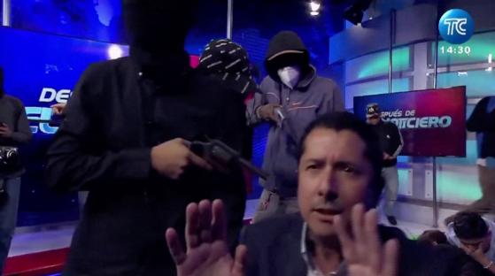 Screengrab of masked men pointing guns at a television presenter during a live broadcast.
