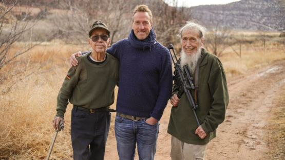 Three men standing outdoors, two older men flanking a younger man.